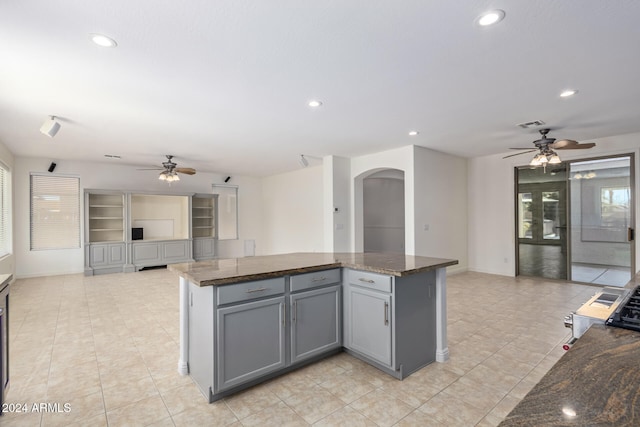 kitchen with light tile patterned floors, a center island, gray cabinets, and dark stone countertops