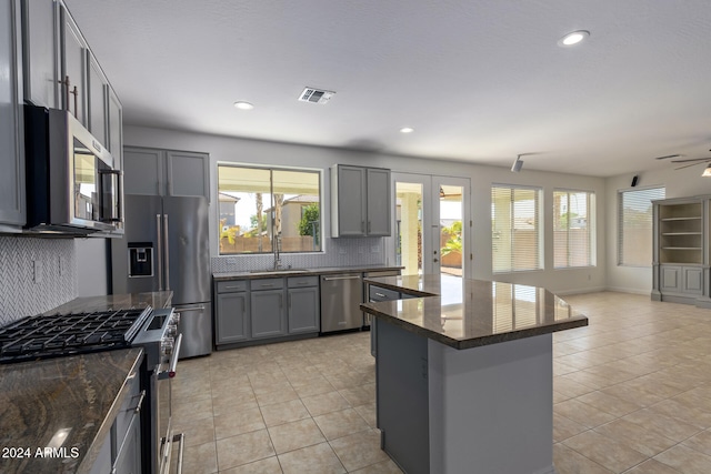 kitchen featuring gray cabinets, stainless steel appliances, a kitchen island, and tasteful backsplash