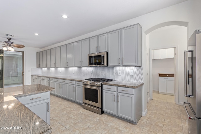 kitchen with arched walkways, stone counters, gray cabinets, and high quality appliances