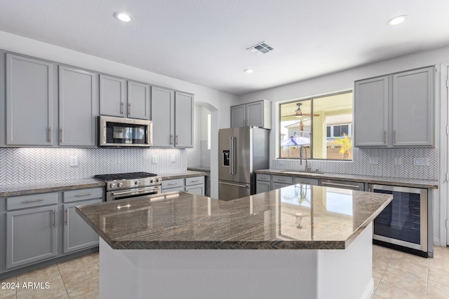 kitchen featuring a center island, high end appliances, dark stone counters, sink, and beverage cooler