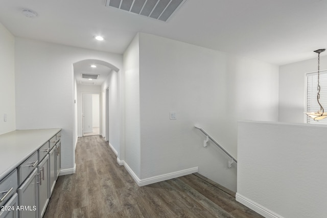 corridor featuring dark wood-type flooring, arched walkways, visible vents, and an upstairs landing