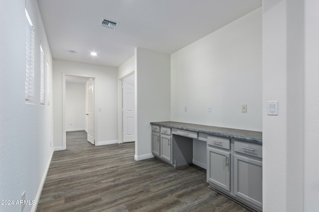 interior space featuring baseboards, dark wood finished floors, dark countertops, gray cabinets, and built in desk