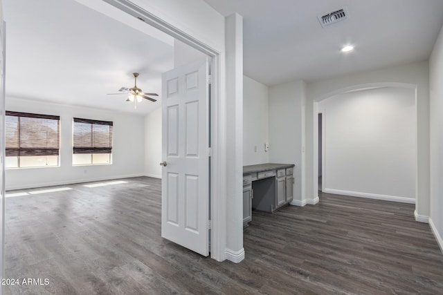 unfurnished living room with ceiling fan, built in desk, and dark wood-type flooring