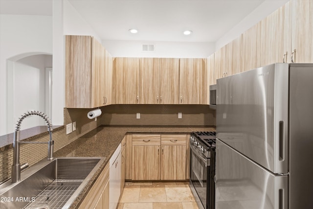 kitchen with dark stone countertops, sink, stainless steel appliances, and light brown cabinets