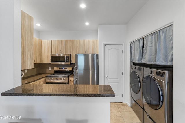 kitchen with washer and dryer, dark stone countertops, light tile patterned floors, kitchen peninsula, and stainless steel appliances