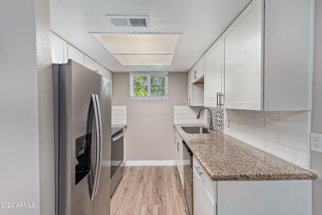 kitchen featuring stainless steel appliances, white cabinetry, dark stone countertops, and sink