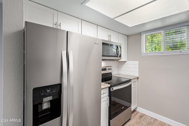 kitchen with white cabinetry, decorative backsplash, stainless steel appliances, light hardwood / wood-style flooring, and light stone countertops