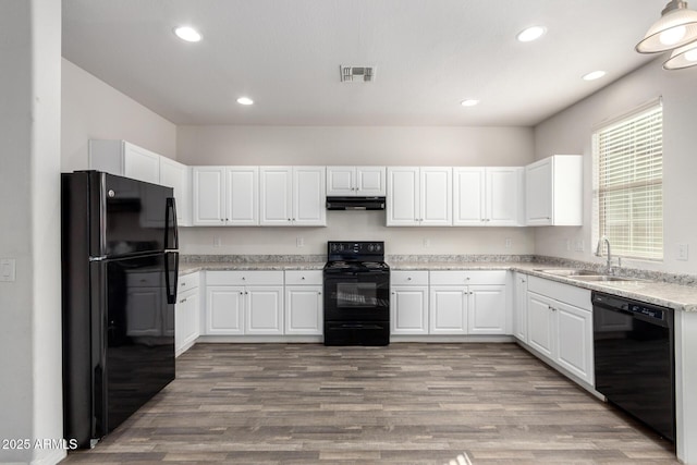 kitchen with black appliances, white cabinets, under cabinet range hood, and a sink