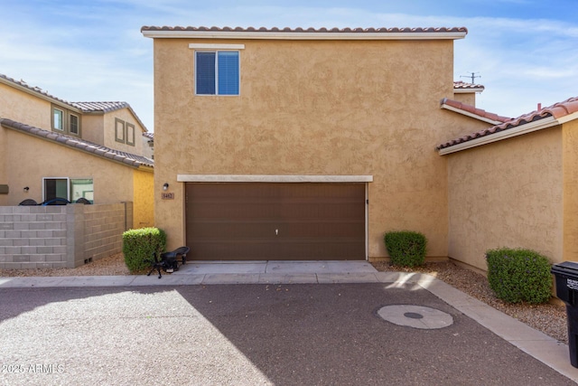 view of front facade with stucco siding, driveway, fence, a garage, and a tiled roof