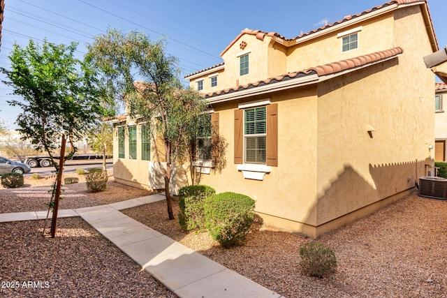 view of side of property with central air condition unit, stucco siding, and a tiled roof