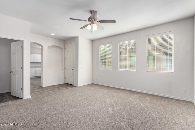 empty room featuring arched walkways, ceiling fan, baseboards, and carpet floors