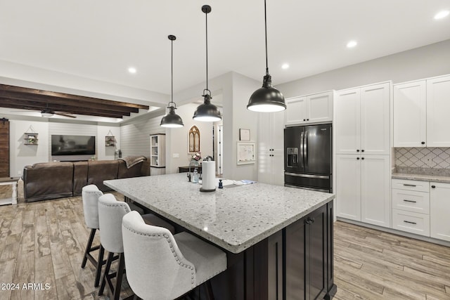 kitchen with pendant lighting, light stone counters, a kitchen island with sink, and black refrigerator with ice dispenser