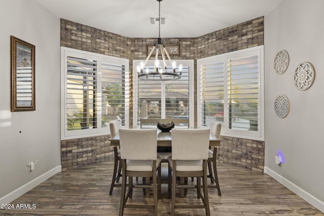 dining area featuring dark hardwood / wood-style flooring, brick wall, and an inviting chandelier