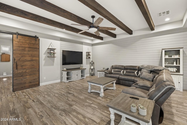 living room featuring ceiling fan, light hardwood / wood-style floors, a barn door, and beamed ceiling