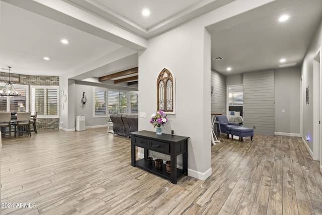 corridor featuring beamed ceiling, an inviting chandelier, and light hardwood / wood-style flooring