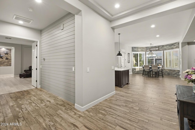 hallway with a notable chandelier, light hardwood / wood-style flooring, and wooden walls