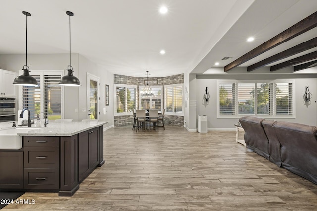 kitchen with hanging light fixtures, sink, light stone counters, and light wood-type flooring