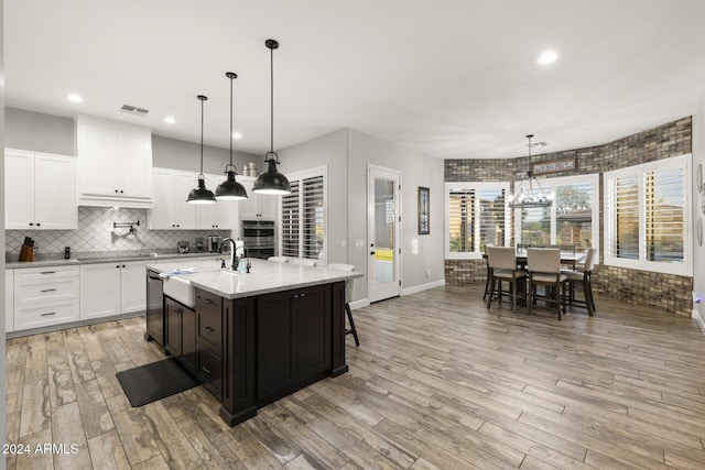 kitchen featuring decorative light fixtures, a center island with sink, light wood-type flooring, dishwasher, and white cabinets