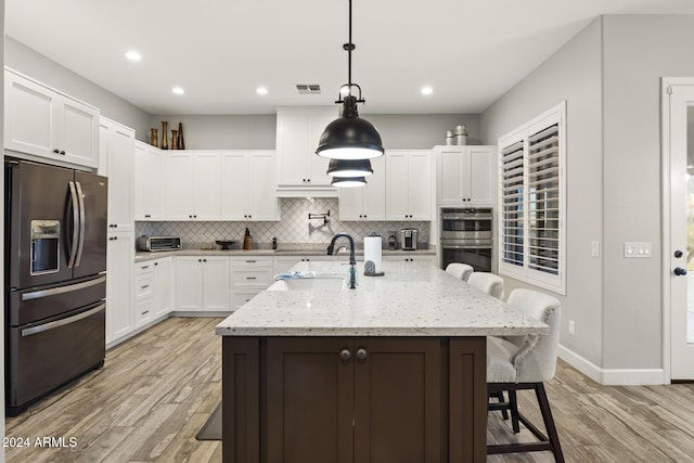 kitchen featuring sink, a breakfast bar area, double oven, hanging light fixtures, and fridge with ice dispenser