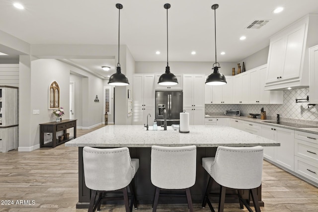 kitchen featuring a kitchen island with sink, stainless steel fridge with ice dispenser, light stone counters, and white cabinets