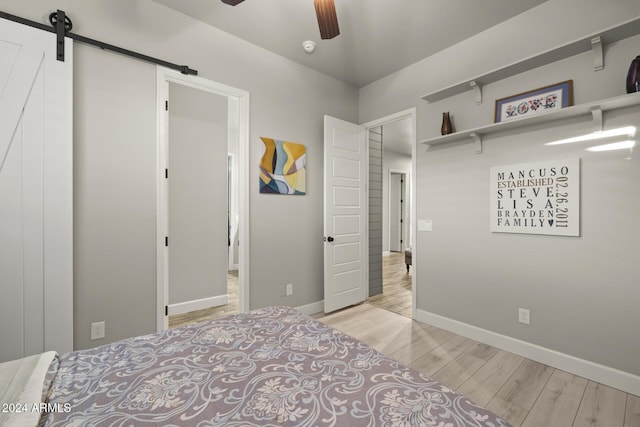 bedroom featuring light hardwood / wood-style flooring, a barn door, and ceiling fan