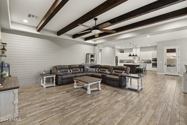 living room with beamed ceiling, ceiling fan, and light hardwood / wood-style flooring