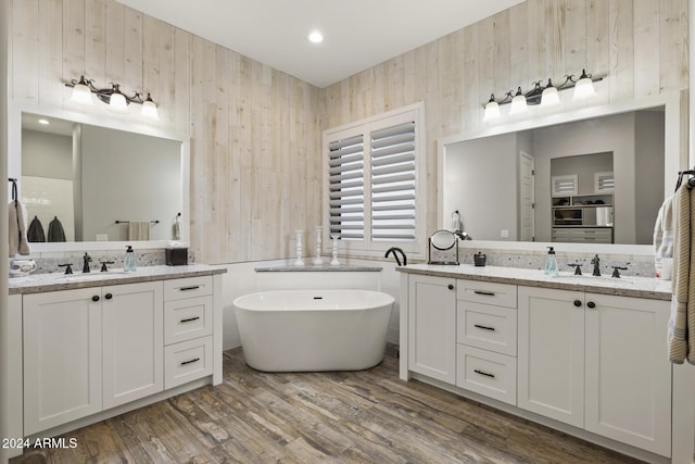 bathroom featuring vanity, wood-type flooring, a bath, and wooden walls