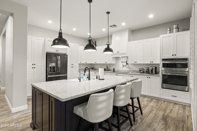 kitchen with white cabinetry, hanging light fixtures, black appliances, and an island with sink