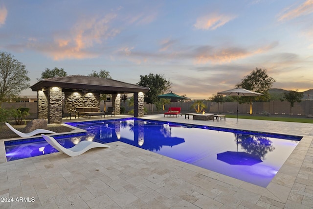 pool at dusk with a gazebo, a patio area, and an outdoor fire pit