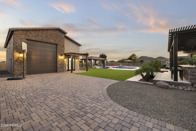 patio terrace at dusk with a yard, a pergola, and a garage