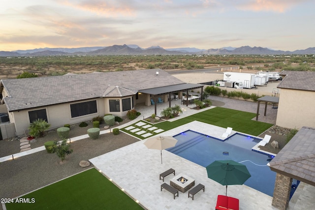 pool at dusk with a mountain view, a fire pit, a patio, and a yard