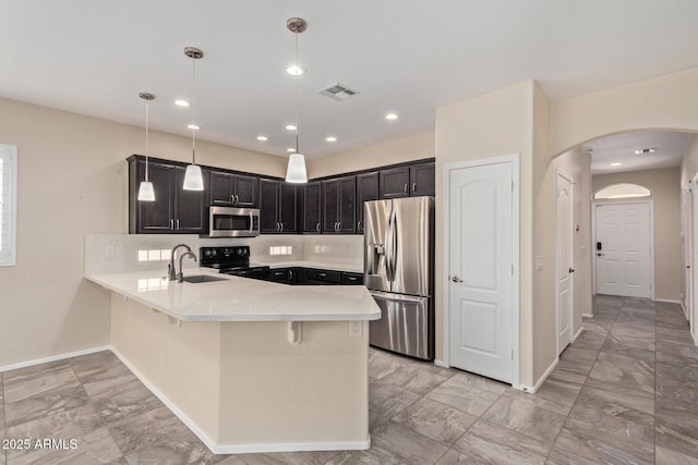 kitchen with appliances with stainless steel finishes, pendant lighting, sink, decorative backsplash, and kitchen peninsula