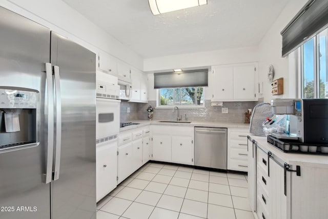 kitchen featuring tasteful backsplash, stainless steel appliances, light countertops, white cabinetry, and a sink