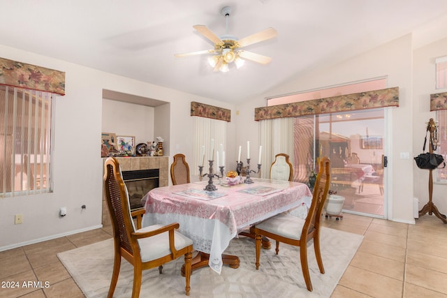 tiled dining space with ceiling fan, a fireplace, a healthy amount of sunlight, and vaulted ceiling