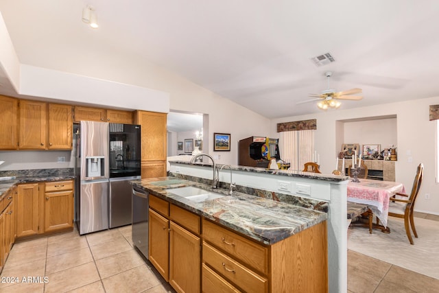 kitchen featuring stainless steel appliances, a kitchen island with sink, ceiling fan, sink, and dark stone countertops