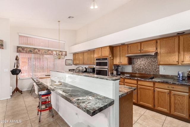 kitchen featuring a center island with sink, vaulted ceiling, decorative light fixtures, light tile patterned flooring, and stainless steel double oven