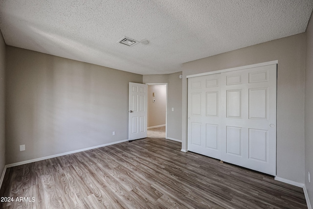 unfurnished bedroom with a textured ceiling, a closet, and hardwood / wood-style flooring