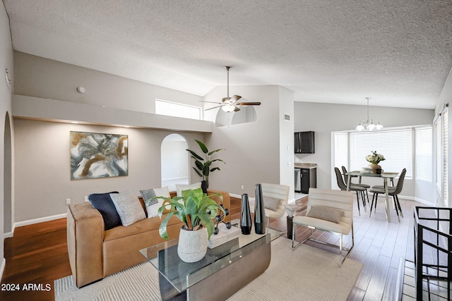 living room with ceiling fan with notable chandelier, vaulted ceiling, a textured ceiling, and wood-type flooring