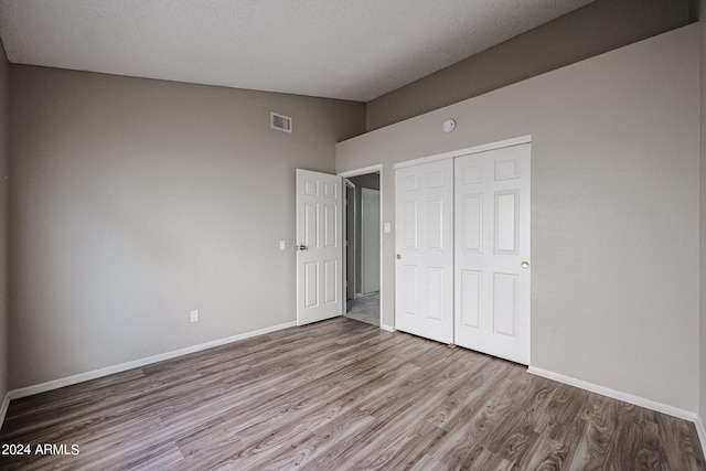 unfurnished bedroom featuring lofted ceiling, a closet, light hardwood / wood-style floors, and a textured ceiling