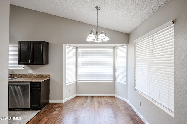 unfurnished dining area featuring a textured ceiling, vaulted ceiling, a notable chandelier, and light hardwood / wood-style floors