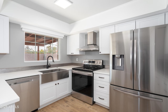 kitchen with appliances with stainless steel finishes, sink, white cabinets, light wood-type flooring, and wall chimney exhaust hood