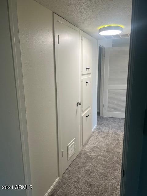 hallway with a textured ceiling and light colored carpet