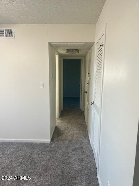 corridor with dark carpet and a textured ceiling