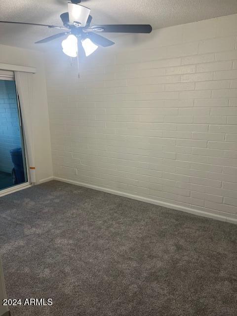 unfurnished room with ceiling fan, brick wall, dark carpet, and a textured ceiling