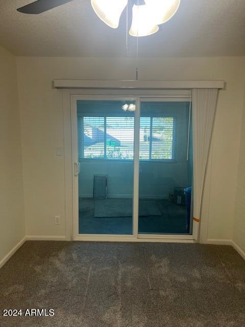 empty room with dark carpet, ceiling fan, and a textured ceiling