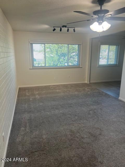 unfurnished room with a textured ceiling, dark colored carpet, rail lighting, and ceiling fan