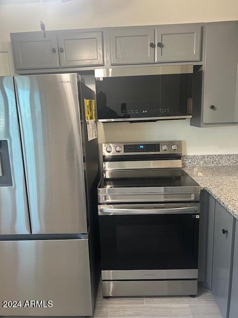 kitchen featuring stainless steel appliances, gray cabinetry, and light stone countertops