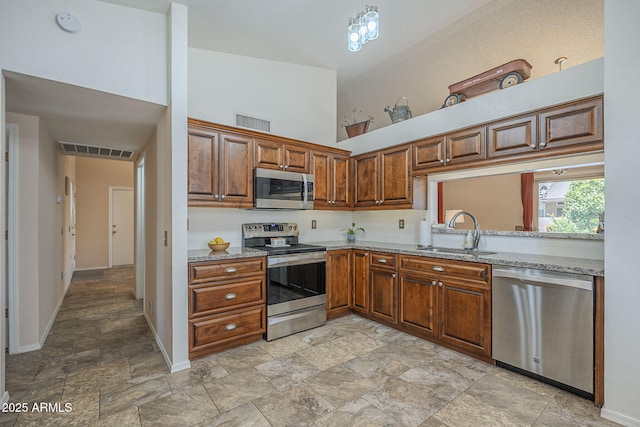 kitchen featuring a sink, a towering ceiling, stainless steel appliances, stone finish flooring, and visible vents