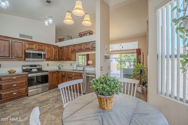kitchen featuring a sink, a towering ceiling, stainless steel appliances, light stone countertops, and visible vents