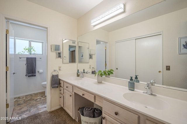 bathroom featuring double vanity, stone finish flooring, toilet, and a sink